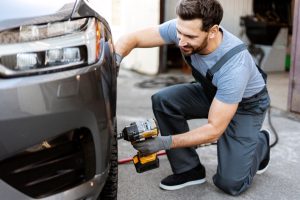 Mechanic changing car tire using electric wrench in auto repair shop